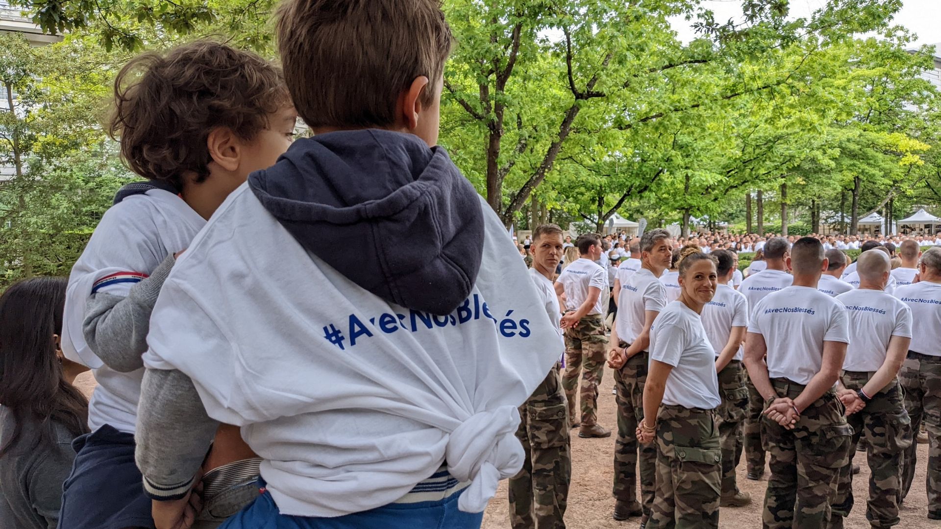 Une militaire adresse un sourire aux enfants derrière elle, qui portent le T-shirt pour l'opération “Avec Nos Blessés”.