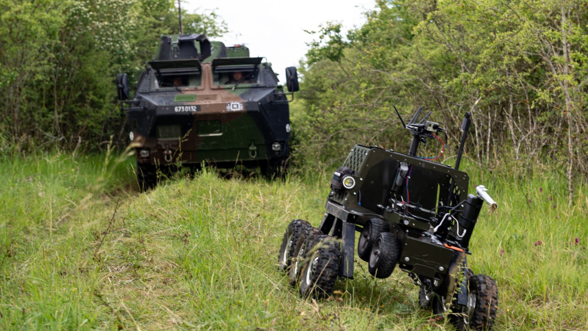 Un char et un robot chariot avancent sur une route de campagne.