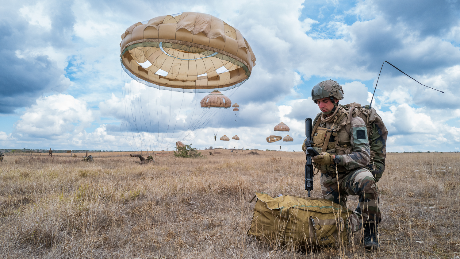 Un parachutiste vérifie son matériel de transmission tandis que le reste de sa section se pose sur la zone de mise à terre à Rodez.