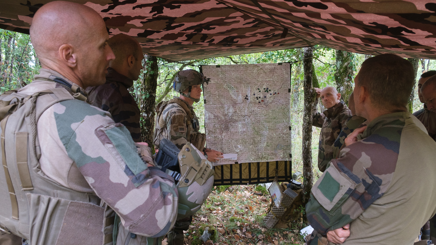 Au milieu des bois, un point de situation est organisé autour d'une carte par les personnels du poste de commandement principal.