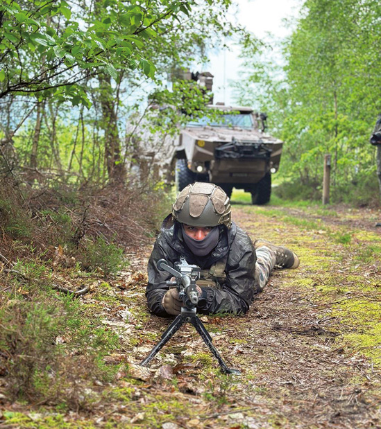 Un soldat est au sol. Armé, il attend patiemment. 