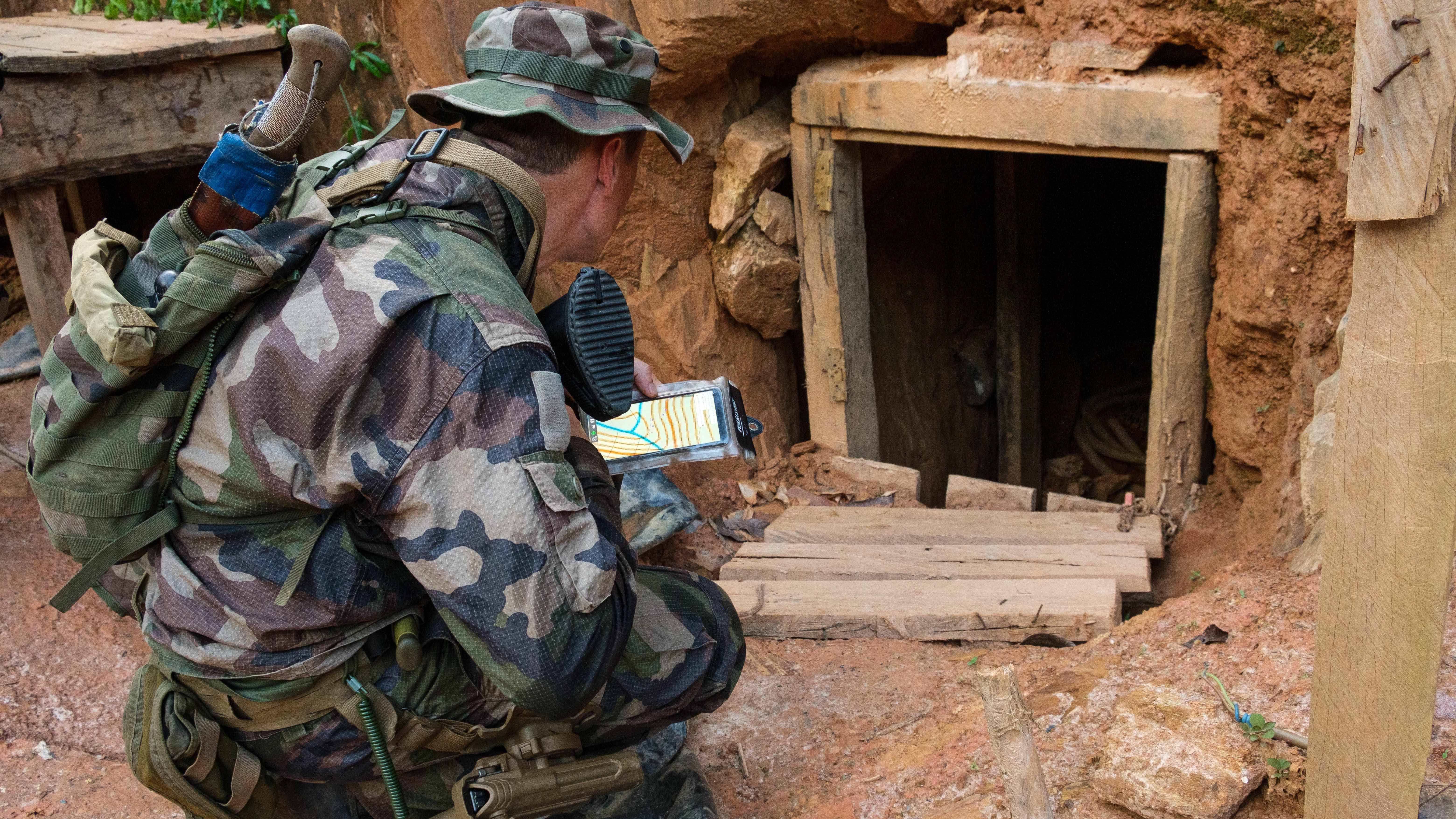 Un militaire français se trouve devant l'entrée d'une galerie d'un site orifère.